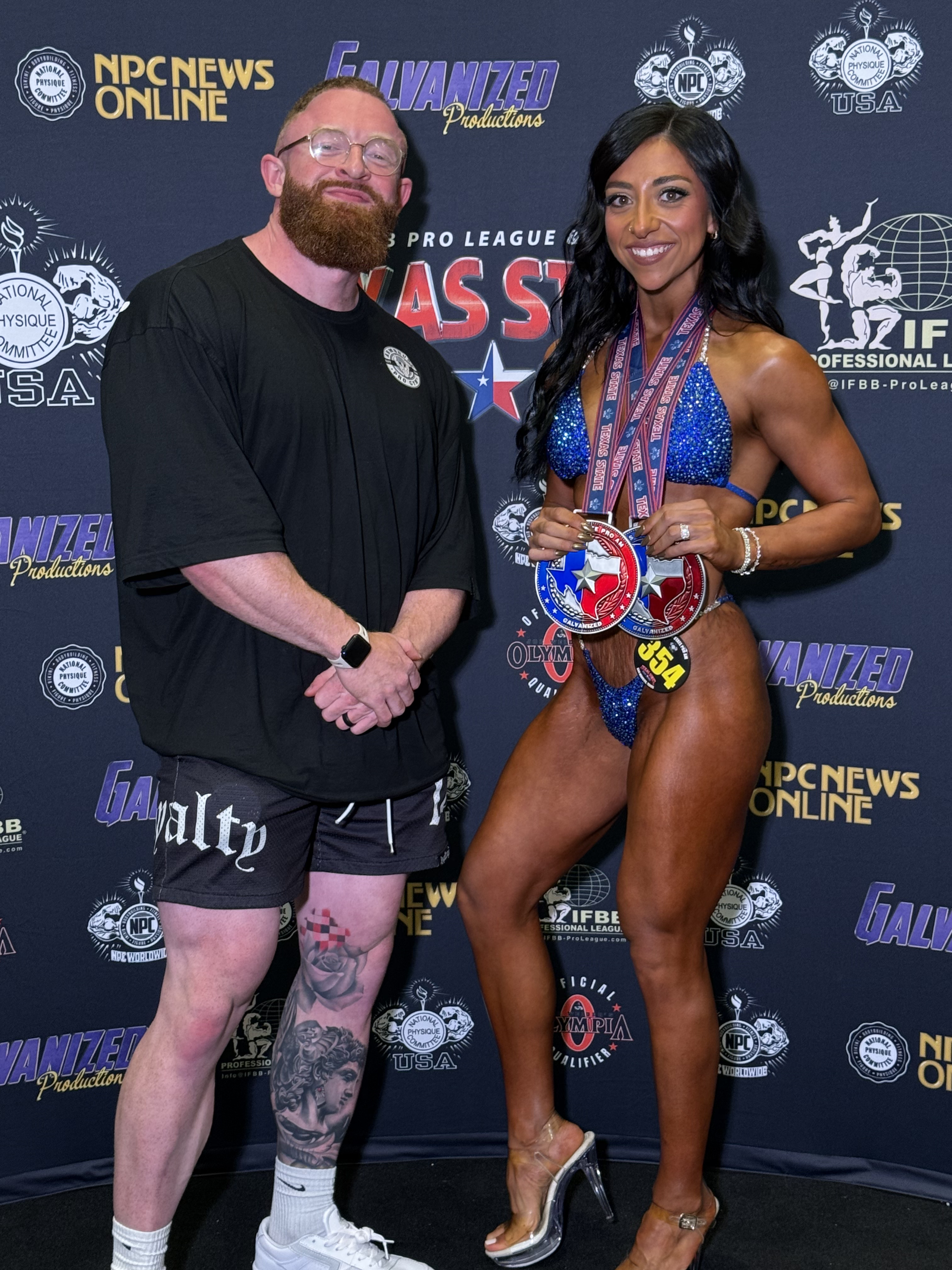 Personal Trainer Marlin Foy stands by a client competing at a bodybuilding competition
